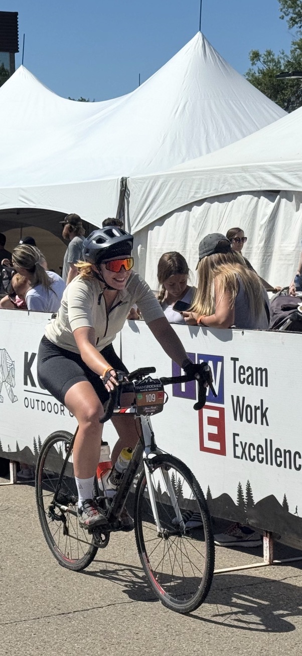 Weronika smiles while cycling across the Gran Fondo Badlands finish line, wearing a helmet and sunglasses.
